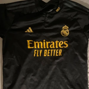 Real Madrid svart fotbollströja Adidas M - Snygg svart Real Madrid fotbollströja från Adidas i slim fit.  Är i väldigt bra skick och använd 1 gång. För salu pga för stor och passar ej mig. Köptes för 899sek