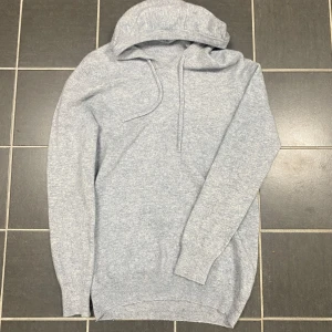 Ljusgrå stickad hoodie i ull - Mysig ljusgrå hoodie i 100% ull med lång ärm och ribbade muddar. Tröjan har huva med snörning och är perfekt för kyliga dagar. Enkel och stilren design som passar till det mesta. Passar från 170-180 cm. Pris kan ej diskuteras.