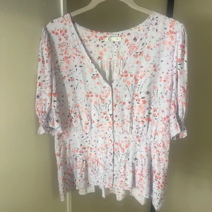 Gullig blommig blus - Superfin blommig blus i ljusa pastellfärger från Cubus. Blusen har v-ringning, knappar framtill, trekvartsärm med resår och volang nertill. Säljer då den inte kommer till användning💞💞