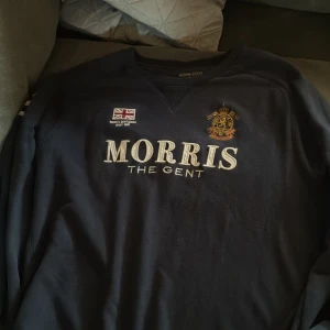 Mörkblå sweatshirt från Morris Gents XL - Mörkblå sweatshirt från Morris Gents i storlek XL. Tröjan har broderad logga, brittisk flagga och siffran 68 på ärmen. Klassisk rund halsringning och ribbade muddar. Snyggt tryck med 'MORRIS THE GENT' framtill.
