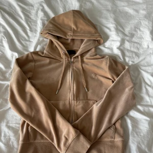 Beige velour hoodie Juicy Couture - Säljer en beige hoodie från Juicy Couture i mjuk velour med huva och snörning. Tröjan har dragkedja framtill, långa ärmar och en liten broderad logga på bröstet. Perfekt för chill dagar men ändå snygg! Använt 1-2 gånger så väldigt bra skick!💕
