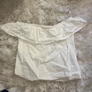 Vit offshoulder topp med volang - Säljer en vit offshoulder topp med bred volangkant runt axlarna. Toppen är ärmlös och har en luftig passform, perfekt för varma dagar. Enkel och stilren design som är lätt att matcha med olika outfits.
