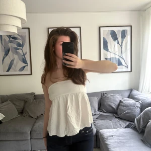 Vit bandeau tubtopp med volang - Säljer en söt vit bandeau tubtopp med volangkant nertill. Perfekt för utgång eller typ vinkväll! Den har en gummi kant högst upp så den sitter bra på plats! Om fler bilder önskas skriv privat!🥰