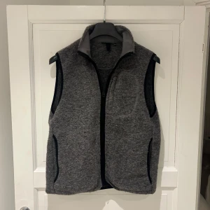 Grå ullväst från J.Lindeberg - Snygg grå väst från J.Lindeberg i mjuk ullmix med hög krage och hel dragkedja framtill. Västen har svarta kantdetaljer, praktiska fickor och en diskret logga i metall på ryggen. Perfekt för lager-på-lager och chill stil.