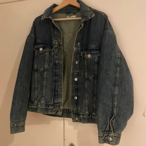 Oversized blå jeansjacka Gina tricot  - Snygg oversized jeansjacka i klassisk blå denim med silverfärgade knappar och två bröstfickor med lock. Jackan har raka linjer, krage och långa ärmar. Perfekt för lager-på-lager och ger en cool vintage vibe till din outfit.