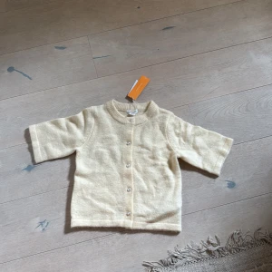 Beige stickad kofta från Gina Tricot - Superfin beige stickad kofta från Gina Tricot Young med pärlknappar framtill. Koftan har ribbad krage och muddar, samt trekvartsärmar som ger en chill vibe. Perfekt att slänga över en t-shirt för extra mysfaktor.