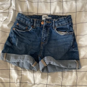 Blå jeansshorts från 157 - Snygga blå jeansshorts från 157 med klassisk femficksdesign, uppvikta ben och gylf med dragkedja. 