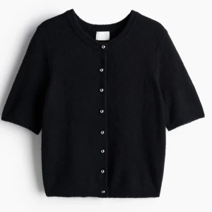 Svart kortärmad kofta med pärlknappar - Kortärmad svart kofta från H&M med rund halsringning och snygga silver pärlknappar framtill. 🩷Koftan är stickad och har en klassisk, enkel look som passar perfekt till jeans eller kjol. Den är lite nopprig med väldigt fin🩷den har också blivit lite uttöjd i ett av knapphålen men går fortfarande att knäppa🩷
