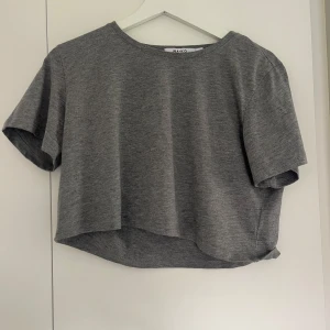 Grå croppad topp från NA-KD - En enkel och stilren grå croppad topp från NA-KD. T-shirten har rund halsringning🩶🩶