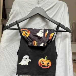 Pyjamassett med spöken och pumpor - En svart linnetopp med smala axelband och tryck av vita spöken och orange pumpor framtill och ett par matchande shorts med rosett till i storlek Xs!! Toppen och shorten har vågig kant nertill och är perfekt för dig som älskar halloween vibes. Materialet är mjukt av polyester. Inga defekter!!! Kontakta mig om du har några funderingar!!❤️