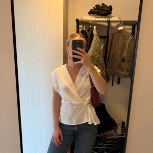 Vit blus Zara - Säljer en vit omlottopp med snygg v-ringning och knyt i midjan. Storlek XS från Zara. Sista bilden är lånad