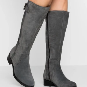 Grå mockastövlar från Anna Field - Snygga knähöga stövlar i grå mocka från Anna Field. De har en låg klack, rund tå och dragkedja på insidan för enkel påtagning. Dekorativt spänne upptill och stilrena sömmar ger en clean look. Perfekta för höst och vinter.