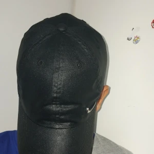 Svart Nike keps Dri-FIT Club Cap - Svart keps från Nike med metalliskt Swoosh-märke framtill och justerbart spänne bak. Tillverkad i Dri-FIT-material som andas och håller dig torr. Klassisk böjd skärm och stilren look, perfekt för sport eller streetwear.