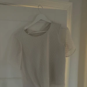 Vit blus - Supersöt vit blus från Lindex med transparenta, korta ärmar och diskret prickigt mönster. Blusen har rund halsringning och är tillverkad i ett lätt, luftigt material🤍