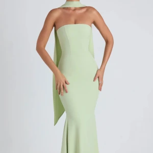 Bal klänning - Supersnygg axelbandslös långklänning i ljusgrönt med figurnära passform och lång cape-detalj som hänger från axlarna. Klänningen har en stilren och elegant siluett, perfekt för dig som vill sticka ut med en modern look. Ohpolly