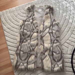 Grå och beige pälsväst från Cream - Säljer en fluffig pälsväst från Cream i grått och beige med coolt mönster. Västen är lång, har mjukt foder och är tillverkad i syntetisk päls av polyester. Perfekt för dig som vill sticka ut med en statement piece.