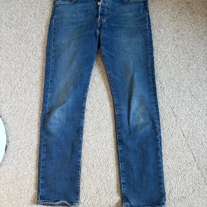 Levi's 501 blå jeans 30/30 - Klassiska blå Levi's 501 jeans med rak passform och knappgylf. Jeansen har en tidlös look med lätt slitning och är tillverkade i robust bomullsdenim. Perfekta för dig som gillar en ikonisk och avslappnad stil.