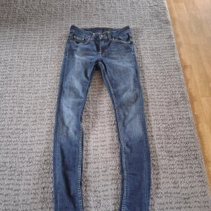Jeans från Tiger of Sweden - Snygga blå jeans från Tiger of Sweden med klassisk femficksdesign och smal passform. Jeansen har gul kontrastsöm, läderpatch bak och är tillverkade i ett mjukt jeanstyg som sitter tajt längs benen. Perfekta för dig som gillar en stilren och modern look.