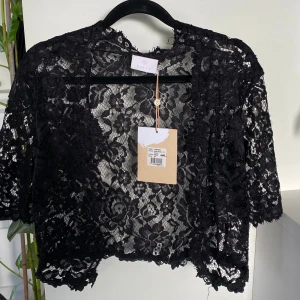 Svart spetstopp / bolero från Kaffe! Ny med prislapp!  - Svart bolerotopp från Kaffe!  Superfin spetstopp/bolero med halvlånga ärmar.Edda heter modellen.  Boleron stängs framtill med en liten hyska! Nypris 449! 