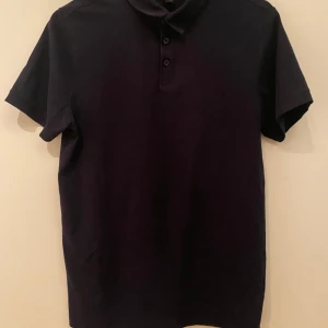 Mörkblå pikétröja från H&M Slim Fit - Mörkblå pikétröja från H&M i slim fit-modell. Klassisk krage med tre knappar framtill och korta ärmar. Tillverkad i mjuk bomull som känns skön mot huden. Perfekt för en clean och stilren look.