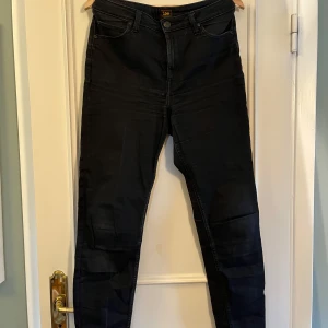 Svarta Scarlett High jeans från Lee - Snygga svarta Scarlett High jeans från Lee med hög midja och klassisk femficksdesign. Jeansen har smal passform och är tillverkade i stretchigt bomullsmaterial för extra komfort. Perfekta för dig som gillar en stilren och enkel look. Skickar fler bilder vid intresse💞