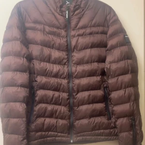 Brun pufferjacka från Replay, L - Snygg brun pufferjacka från Replay i storlek L. Jackan har quiltad design, dragkedja framtill och två sidofickor med svarta dragkedjor. Insidan är grå med gul detalj och Replay-logga på ärmen. Perfekt för kalla dagar och har en modern, loose       Fint skick förutom en en tråd som gått upp  (se foton för skick )  Inget annat att anmärka på