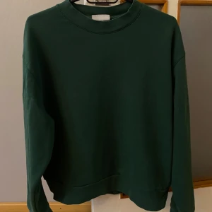 Mörkgrön sweatshirt från Weekday XS - En stilren mörkgrön sweatshirt från Weekday i storlek XS. Tröjan har en klassisk rund halsringning och långa ärmar. Perfekt för dig som gillar en enkel och clean look. Tillverkad i mjuk bomull för skön komfort.