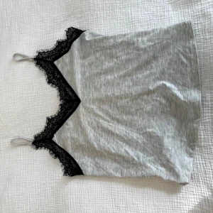 Grå linnetopp med svart spetskant - Snygg grå linnetopp med tunna axelband och dekorativ svart spets längs v-ringningen.💘                  Aldrig använt, i strl S💘                                                         Skickar ditt köp inom 24h!💘