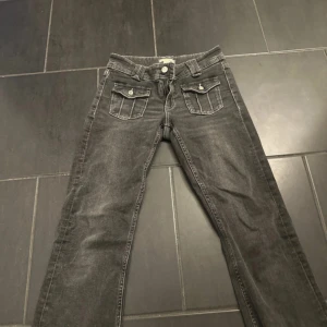 Grå jeans med fickdetaljer fram - Snygga grå jeans med raka ben och coola fickor med lock och knapp framtill. Klassisk femficksmodell med bälteshällor och dragkedja. Perfekta för dig som gillar en avslappnad men ändå stilren look.