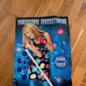 Hannah Montana Make it Rock - Färgstark och glittrig Hannah Montana-affisch från 2008! Perfekt för dig som älskar musik, popkultur och vill ge ditt rum en cool superstar-vibe. Motivet visar Hannah med mikrofon och energi – en riktig ikon för unga fans.