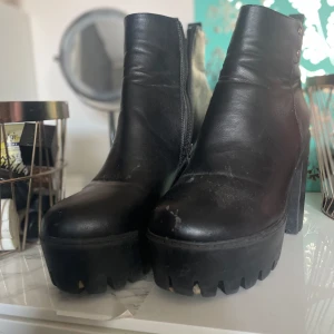 Svarta chunky boots med klack - Säljer ett par svarta boots i skinnimitation med grov platåsula och hög klack. Skorna har rund tå, dragkedja på insidan och nitar vid skaftet. Perfekta för dig som gillar en edgy och trendig stil.