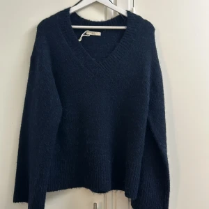 Mörkblå stickad tröja från Gina Tricot - Mysig mörkblå stickad tröja från Gina Tricot med v-ringning och ribbade muddar. Tröjan har lång ärm och en lite loose passform, perfekt för lager på lager under kyliga dagar. Enkel och stilren design som funkar till allt.