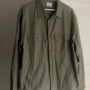 Mörkgrön overshirt från H&M - Mörkgrön overshirt från H&M i relaxed fit. Riktigt fet overshirt. Skjortan har två bröstfickor med lock och knappar, klassisk krage och knäppning framtill. Perfekt lager-på-lager-plagg med lång ärm och enkel, stilren design.