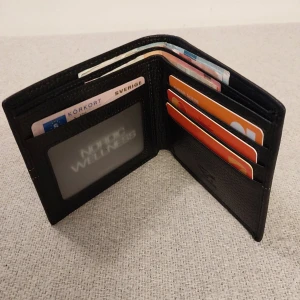 Svart plånbok i skinn från Septwolves - Ny  - Ny och högt kvalitet, Stilren svart plånbok från Septwolves i äkta skinn med präglad yta. Plånboken har flera kortfack, fönster för ID-kort och plats för sedlar. Snygg detalj med logotyp och kontrastsöm på framsidan. Levereras i exklusiv presentförpackning.