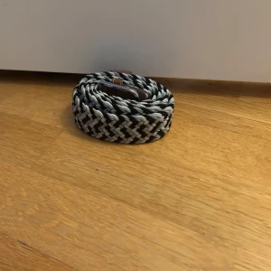Svart och grått flätat bälte - Snyggt flätat bälte i svart och grått med bruna skinn-detaljer vid spännet. Bältet har ett coolt mönster och passar perfekt till jeans. Nypris ca 350 kr
