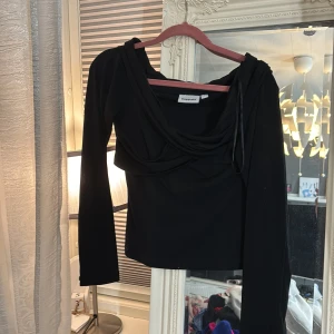 Svart långärmad topp från Kappahl - Svart långärmad topp från Kappahl med draperad halsringning och cool asymmetrisk detalj framtill. Super snygg och oanvänd!❣️