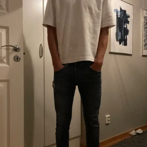 Mörkblå slim jeans med slitningar - Dondup George  - Säljer ett par mörkblå slim jeans med snygga slitningar på låret och knät. Jeansen har klassisk femficksdesign, smal passform och är tillverkade i stretchigt denim för extra komfort. Perfekta för dig som gillar en slim och modern look.