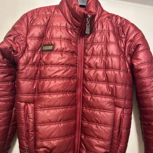 Röd puffer jacka från Calvin Klein - Säljer en snygg röd pufferjacka från Calvin Klein Jeans i storlek M. Jackan har quiltad design, hög krage och dragkedja framtill. Märkesdetalj på bröstet och två fickor med dragkedja. Perfekt för kyligare dagar och riktigt skön att bära.