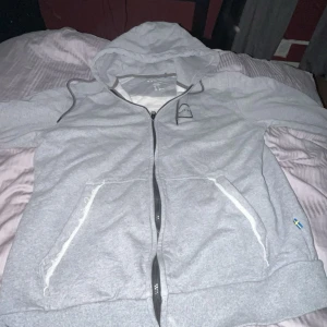 Grå Volvo hoodie XL men passformen som L - Säljer en grå hoodie från Volvo i storlek L. Tröjan har huva med snörning, hel dragkedja och två fickor framtill. Volvo-logga tryckt på både bröstet och ryggen. Tillverkad i mjuk bomullsmix, perfekt för chill dagar.