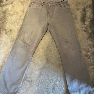 Grå Levi's 501 jeans straight fit - Säljer ett par grå Levi's 501 jeans med klassisk rak passform och fem fickor. Byxorna har knappgylf, bälteshällor och den ikoniska läderpatchen bak i midjan. Tillverkade i slitstarkt bomullstyg och passar perfekt till en avslappnad stil.