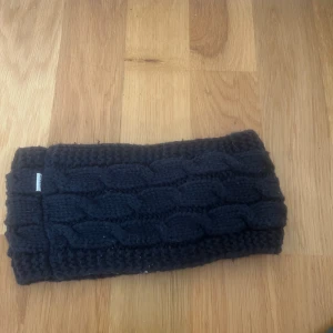 Svart stickat pannband från Sätila - Svart stickat pannband från hööks med grov kabelstickning. Perfekt för kalla dagar när du vill hålla öronen varma utan att bära mössa. Tjockt och mjukt material som sitter skönt runt huvudet.