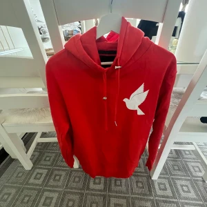 Röd hoodie från GalagoWear med duva - Röd hoodie från GalagoWear med vit duva tryckt på bröstet. Tröjan har huva med snörning, långa ärmar och ribbade muddar. Perfekt för dig som gillar streetstyle och vill sticka ut med en snygg detalj framtill.har 3 st , alla för 250kr