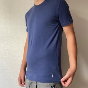 Blå t-shirt från Polo Ralph Lauren - Säljer en stilren blå t-shirt från Polo Ralph Lauren med klassisk passform och korta ärmar. T-shirten har rund halsringning och den ikoniska broderade loggan i vitt nertill. Tillverkad i mjuk bomull som är skön mot huden. Modellen är 176cm