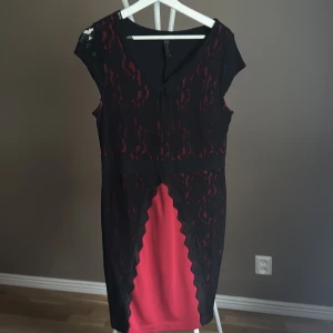 Svart och röd spetsklänning från Rainbow - Supersnygg svart och röd kortklänning från Rainbow med spetsdetaljer och v-ringning. Klänningen har figurnära passform, är ärmlös och har ett coolt mönster med svart spets över rött tyg framtill. Perfekt för dig som vill sticka ut med en edgy look.