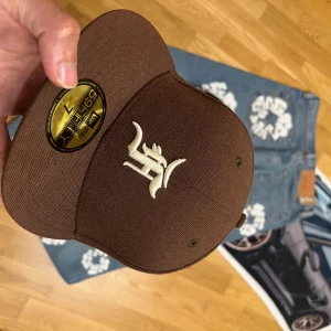 Brun New Era Essentials keps i ull - Säljer en brun fitted keps från New Era Essentials, modell 59FIFTY. Kepsen är i 100% ull och har broderad logga framtill i vitt samt diskret New Era-brodyr på sidan. Klassisk rak skärm och stilren look, perfekt för dig som gillar streetwear.