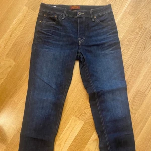 Mörkblå jeans Jack & Jones  31/30 - Snygga mörkblå jeans från Jack & Jones, modell Clark Regular. Klassisk femficksdesign med kontrastsömmar och raka ben. Jeansen är tillverkade i slitstarkt bomullstyg och har en stilren look som passar till det mesta. Helt nya har använt 2gånger