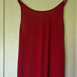 Rött linne med snörning i ryggen - Rött linne i storlek L med tunna axelband som sen utvecklas till korsningar i ryggen. Tillverkad i en mjuk blandning av bomull och polyester som känns lätt och skön. Perfekt för dig som gillar en enkel design med en extra detalj.
