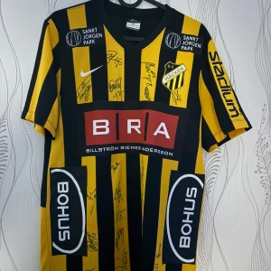 BK Häcken signerad matchtröja Nike - BK Häcken 2016-2017 fotbollströja från Nike med svarta och gula vertikala ränder, klubbmärke på bröstet och flera sponsorloggor. Tröjan är signerad av spelare och har tryckta namn på ryggen. Klassisk passform i lätt funktionsmaterial, perfekt för fans. m