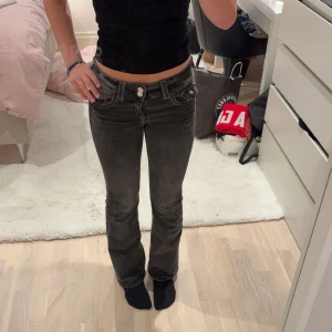Svarta bootcut jeans med låg midja från Gina - Säljer ett par svarta jeans med snygg bootcut och låg midja. Jeansen har klassiska fickor fram och bak, dubbla knappar och dragkedja. Från Gina young storlek 158, jag e 164 cm lång