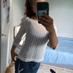 Vit broderad blus med knappar - Superfin vit blus i bomull med broderade hålmönster och knappar längs ryggen. Blusen har trekvartsärm och en rak, lite loose passform. Perfekt för dig som gillar romantiska detaljer och en luftig känsla.